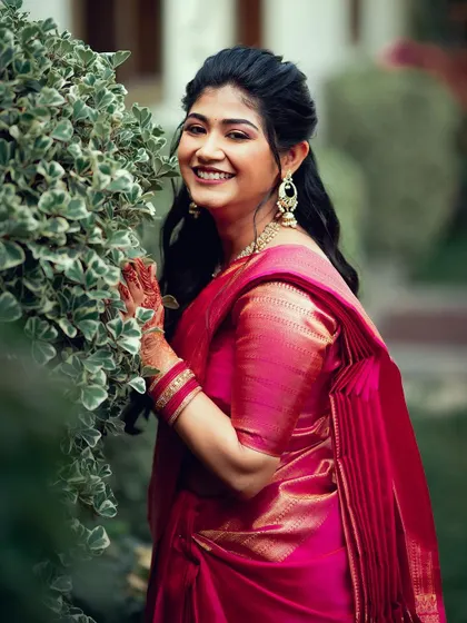 A radiant bride-to-be in a vibrant pink saree, smiling in a beautiful garden setting before her engagement.