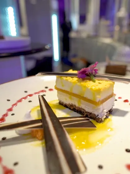 A slice of our layered mango cheesecake, artfully plated with chocolate garnishes and fruit coulis. This dessert is a perfect balance of creamy, fruity, and decadent flavours.