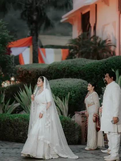 The bride, accompanied by her family, walks with grace and poise, her long veil trailing behind her in this elegant, candid moment.