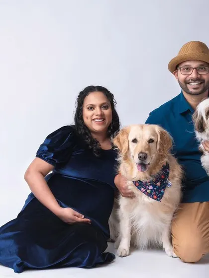 A happy family portrait featuring the expecting couple and their two dogs, a golden retriever and a shih tzu. This studio shot captures the joy and excitement of the entire family, including the furry members, as they await their new arrival.