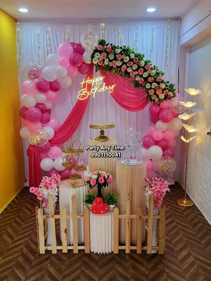 A vibrant pink floral and balloon arch decoration in my party hall, featuring a small picket fence and elegant plinths.