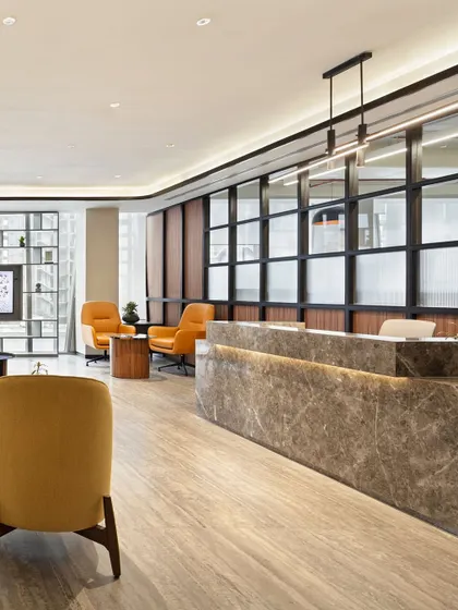 The reception area of a modern office, featuring a marble-clad desk and warm, inviting seating. This space is designed to be the perfect first touchpoint, blending professional aesthetics with a sense of comfort and hospitality.