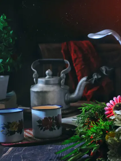 A dark and moody still life of a vintage tea set, complete with an old kettle and floral mugs. The dramatic lighting creates a nostalgic and atmospheric scene.