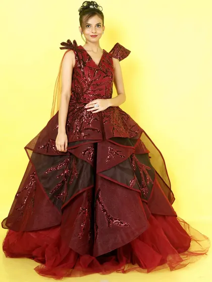 A full view of the dramatic maroon and black structured ballgown. The architectural layers and sequin embellishments make it a work of art.