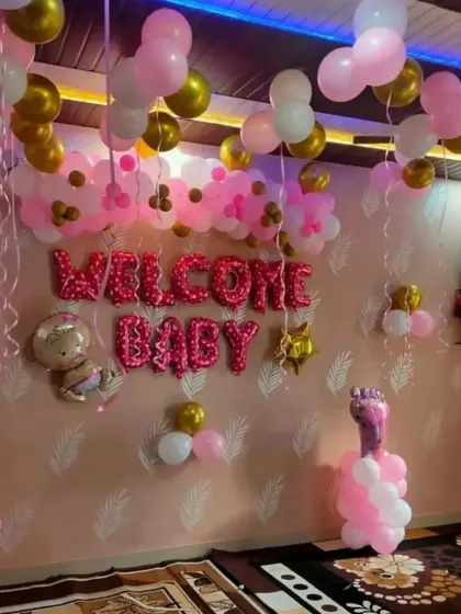 A 'Welcome Baby' room decoration with pink and gold balloons and foil letters.