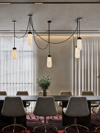 Lighting can define a room. In this boardroom, a custom pendant fixture with cascading lights creates a dramatic focal point over the main conference table, adding a touch of modern elegance to the space.