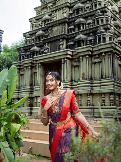 A stunning shot of a bride in a purple and red silk saree, set against a temple, creating a look of timeless grace.