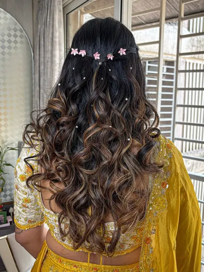 A beautiful half-up hairstyle with bouncy curls and delicate pink flower accessories for a fresh look.