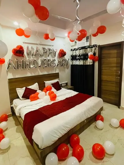 A simple and clean anniversary room decoration with red and white balloons and a "Happy Anniversary" foil balloon banner.