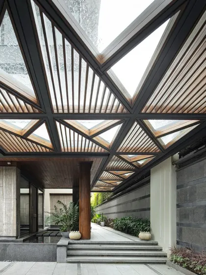 An alternate view of the Bammi Residence entrance, showcasing the interplay between the strong architectural lines of the canopy, the lush landscaping, and the tranquil water feature. This composition of wood, stone, water, and greenery establishes the home's core theme of harmony between built form and nature.