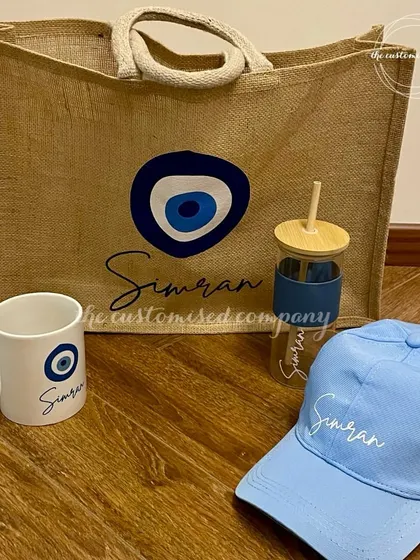 All things evil eye. This coordinated set includes a personalized jute tote bag, a coffee mug, a glass tumbler, and a baseball cap, all featuring the protective symbol.