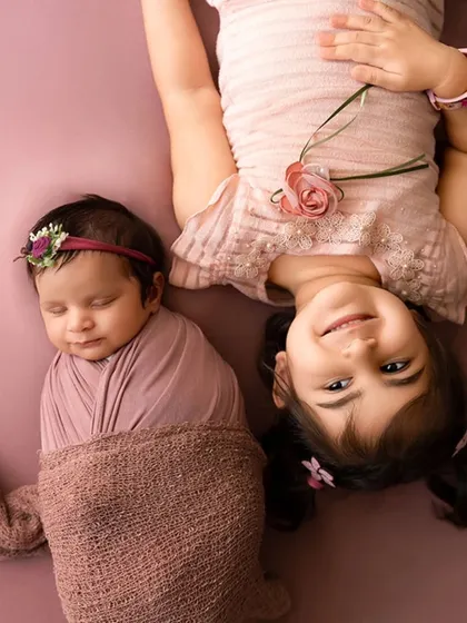 An older sister lies next to her sleeping newborn sibling, a tender moment captured during a newborn session.