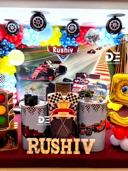 A high-octane Formula 1 racing theme for Rushiv's 5th birthday. The decor includes a racetrack backdrop, a traffic light prop, and a giant number '5' balloon.