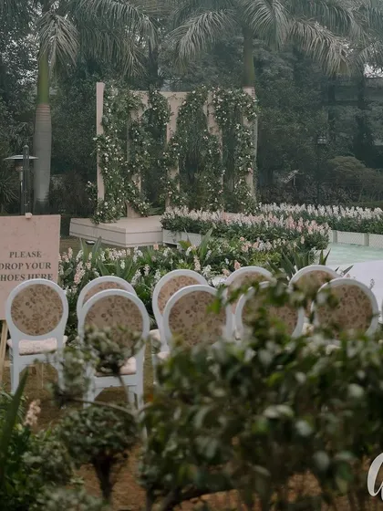 The entrance to the ceremony, with a simple sign asking guests to remove their shoes. The aisle is lined with white flowers, leading to a stage decorated with climbing greenery.