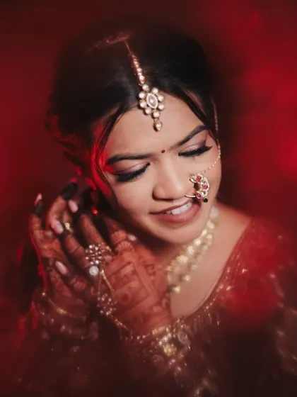 A close-up portrait of the bride in her deep red wedding lehenga. The makeup features a soft smokey eye and a natural lip, creating a look that is both classic and modern.