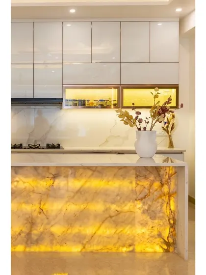 A close-up of the luxurious kitchen with the backlit onyx island. This view highlights the glossy white cabinets and the warm glow from the under-cabinet lighting, which creates a sophisticated and inviting ambiance.