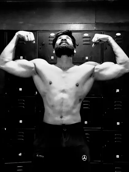 A powerful black and white shot, flexing in front of the gym lockers. The Mercedes logo on the shorts is a nice touch.