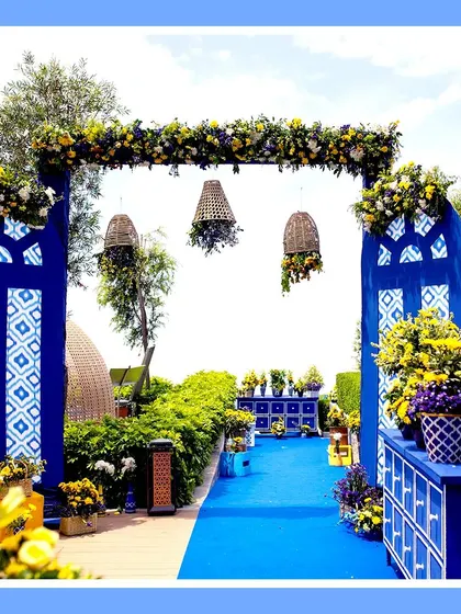 A grand entranceway for a blue and yellow themed Haldi. The structures are painted a deep royal blue with traditional patterns, complemented by large arrangements of yellow flowers.