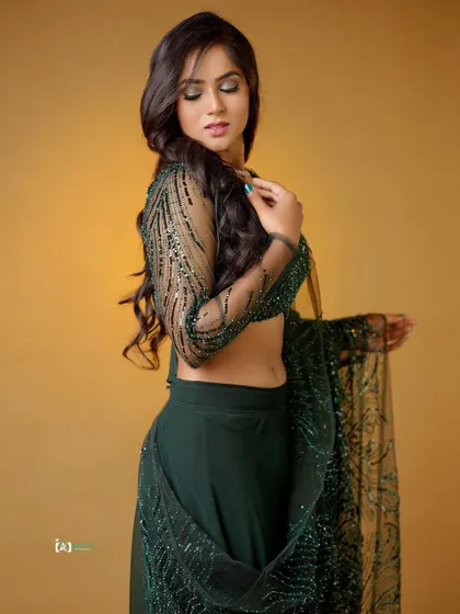This pose highlights the midriff and the intricate embroidery on the blouse. The lighting is designed to sculpt the body and showcase the details of the outfit.