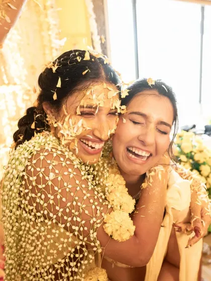 A heartfelt hug between the bride and her sister, both covered in haldi and flowers. A beautiful, emotional moment amidst the fun.