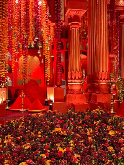 The base of the mandap pillars, surrounded by a garden of red and orange marigolds, creating the feeling that the structure is rising from a field of flowers.