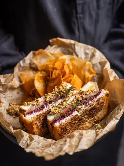 A delightful Ham and Cheese sandwich, perfectly grilled and served with a side of house-made chips. It’s a classic done right, ideal for a satisfying and delicious breakfast.