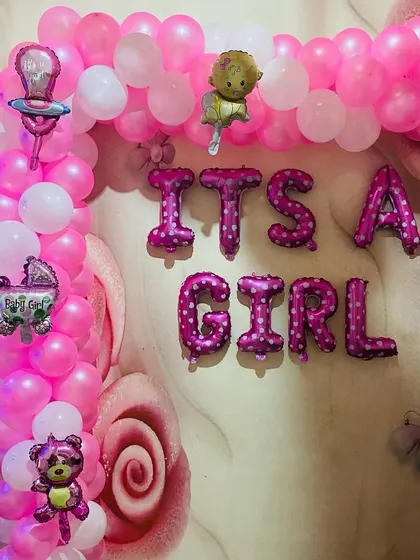 An "It's a Girl" welcome baby decoration with a pink balloon arch and various baby-themed foil balloons.
