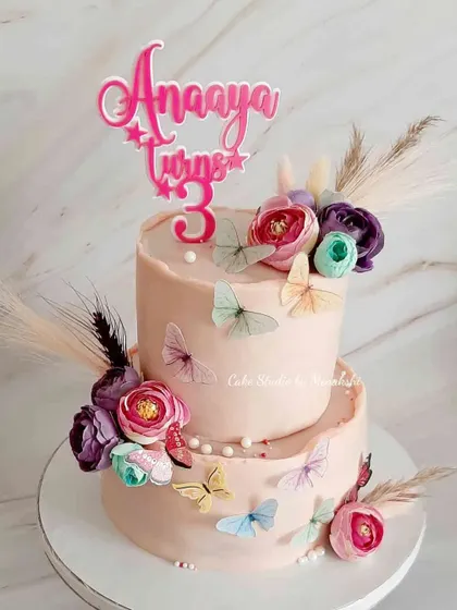 A pretty two-tier floral and butterfly cake for a third birthday. This is a zero-fondant cake, using soft pink buttercream as a canvas for the delicate decorations.