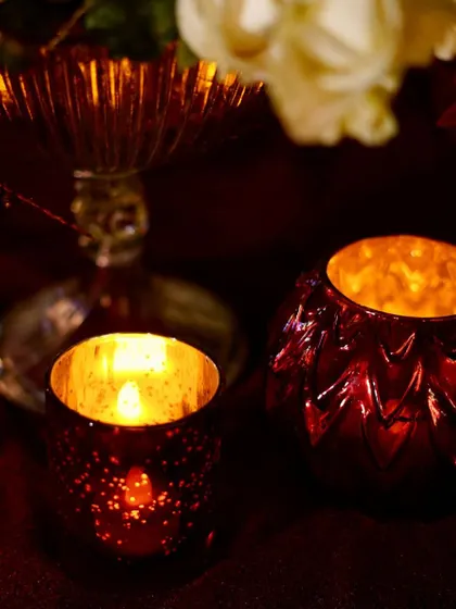 A close-up of the beautiful red mercury glass candle holders, which cast a warm, dappled light, adding to the romantic and regal charm of the evening.