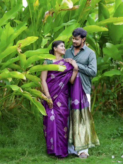 An intimate moment captured amidst lush greenery. The rich purple saree stands out beautifully against the natural background.