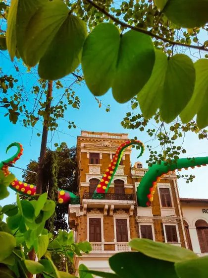 A whimsical installation of giant, colorful octopus tentacles emerging from the windows of a classic old building in Mumbai. A surreal and playful piece of public art.