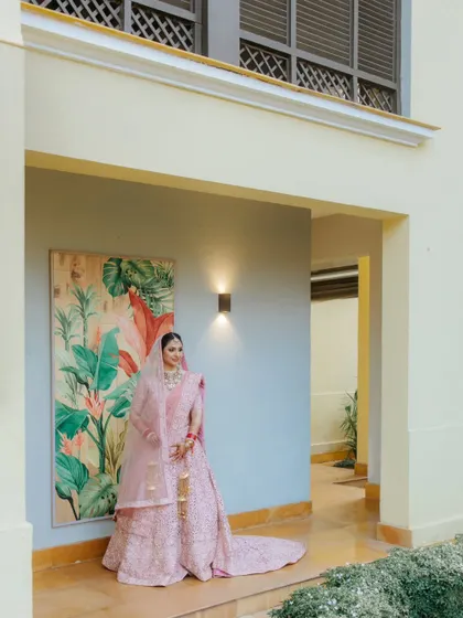 A full-length portrait of the bride Ashrika in her pastel pink lehenga, looking serene and elegant at her Goa wedding venue.