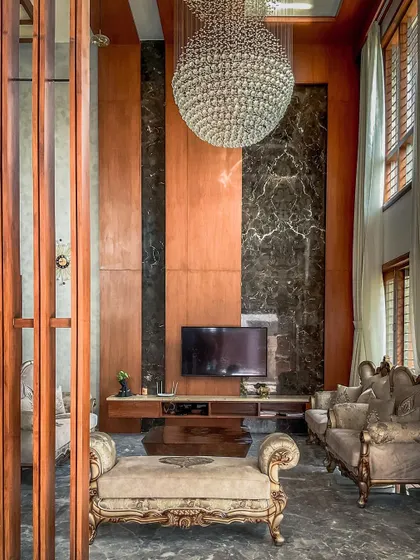 The entertainment zone in the living room is framed by floor-to-ceiling wood and marble panels. This composition creates a sophisticated backdrop for the television, integrating technology seamlessly into the luxurious decor.