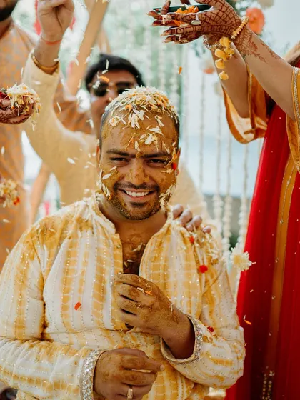 The groom gets showered with turmeric and flower petals by his loved ones during a fun-filled Haldi ceremony.