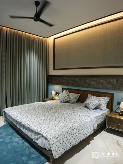 A serene bedroom setting with a custom wooden bed and integrated headboard. The cool blue and white bedding contrasts beautifully with the warm wood tones and full-length curtains.