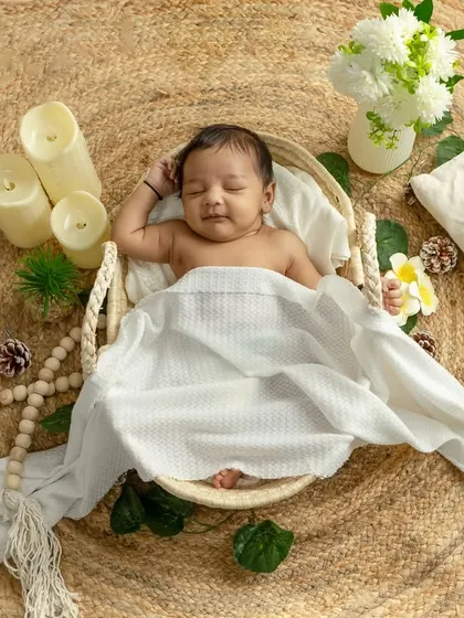 A peaceful sleeping portrait with a beautiful boho aesthetic. The baby is lightly covered with a white blanket, surrounded by candles and natural textures.