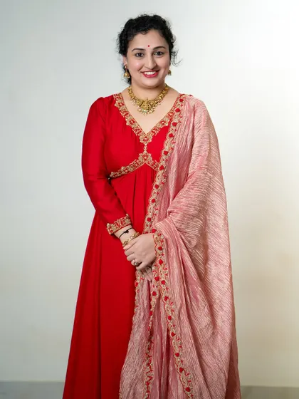 A smiling portrait of Pragathi Rishab Shetty in the red Anarkali, looking effortlessly elegant.