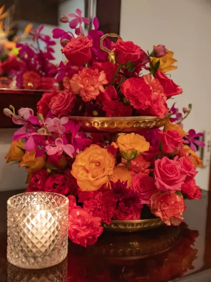 A two-tiered stand holds a cascade of orange and pink roses and carnations. This is a beautiful and space-efficient way to add a pop of color to a smaller table or bar area.