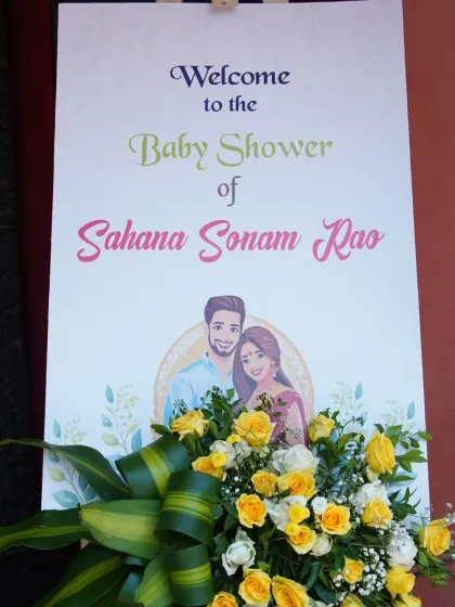 A personalized welcome sign for Sahana Sonam Rao's baby shower, complete with a caricature of the couple and a yellow floral arrangement.
