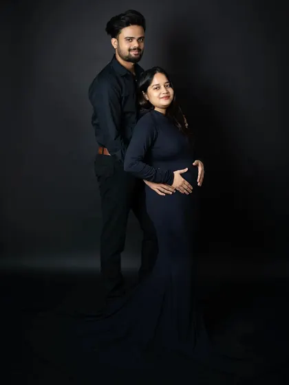 A timeless and elegant couple's portrait. The coordinated black outfits against a dark backdrop create a sophisticated look that focuses all the attention on the expecting parents.