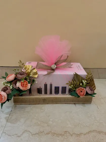 Simple, elegant, and beautiful wedding gift wrapping. A pink box is placed on a wooden platter and decorated with a soft tulle bow and floral arrangements on each side.