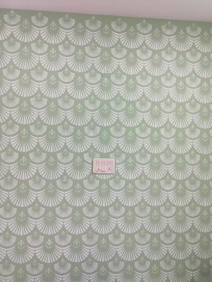 This full accent wall is covered in an art deco-inspired fan or shell stencil pattern. The repetitive design in a soft green creates a stylish and calming effect, perfect for a bedroom or study.