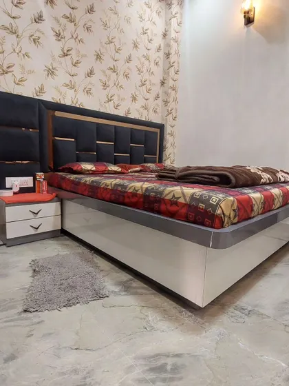 A simple and beautiful bed design. The dark upholstered headboard with gold trim contrasts nicely with the floral wallpaper, creating a classic and elegant look.