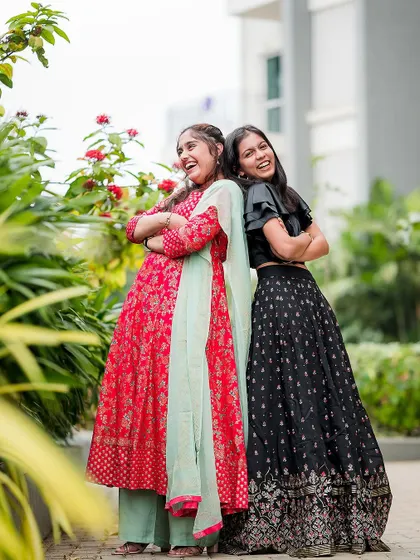 Two sisters laughing and posing back-to-back in a garden. Their coordinated outfits and joyful expressions make this a perfect sibling portrait.