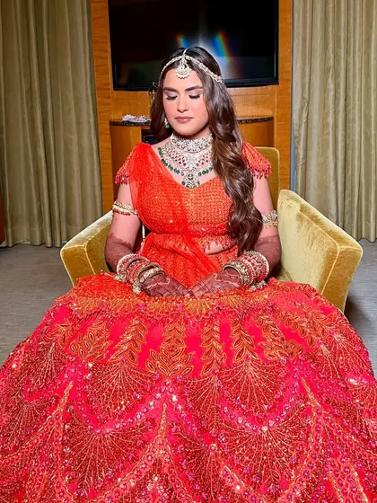 Seated like a queen, ready for her big moment. This look was about creating a dreamy, ethereal vibe with soft makeup that complemented her vibrant red and orange lehenga.