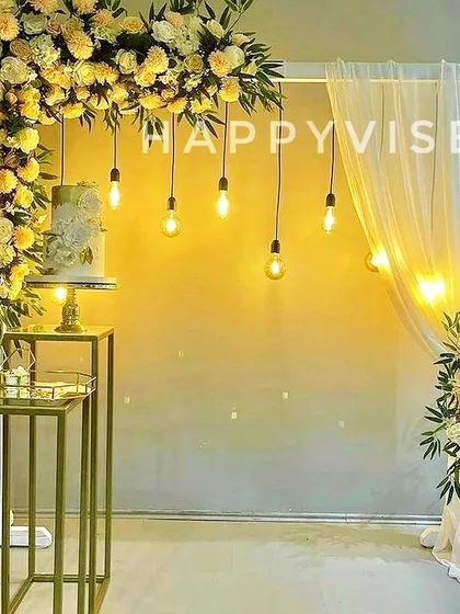 A modern and minimalist decor idea, this setup combines a cascade of yellow and white flowers with hanging Edison bulbs. It’s a chic backdrop for a cake-cutting ceremony or engagement.
