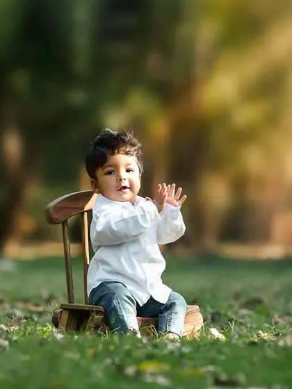 A toddler sits on a small chair in a park, a simple and beautiful outdoor portrait.