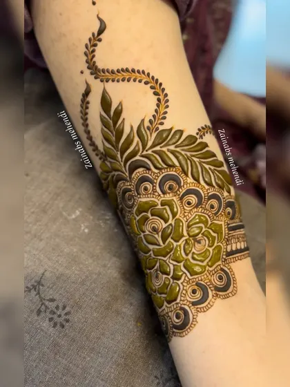 A close-up of the fresh henna paste on Ameena's arm, showcasing a beautiful Pakistani design with bold leaves and roses.