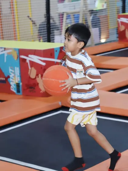 A young boy walks across the trampoline court with a basketball, ready for his next game.