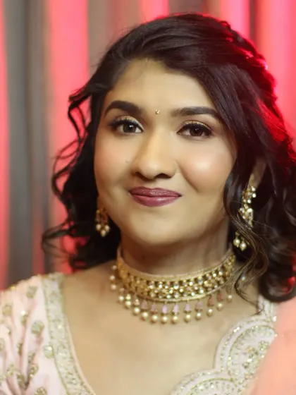 A close-up portrait showcasing her modern glam makeup. The look features beautifully blended eyeshadow, defined brows, and a deep mauve lipstick.